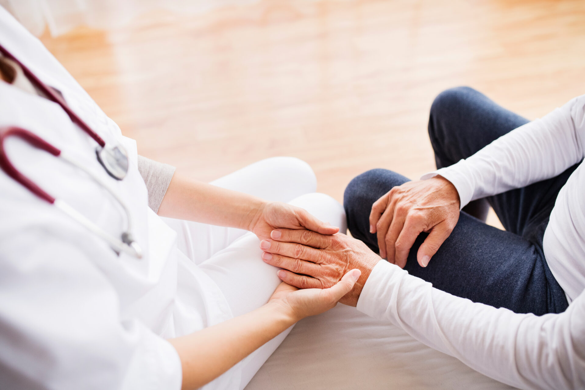 Close up on two people holding hands. One has a stethoscope around their neck.