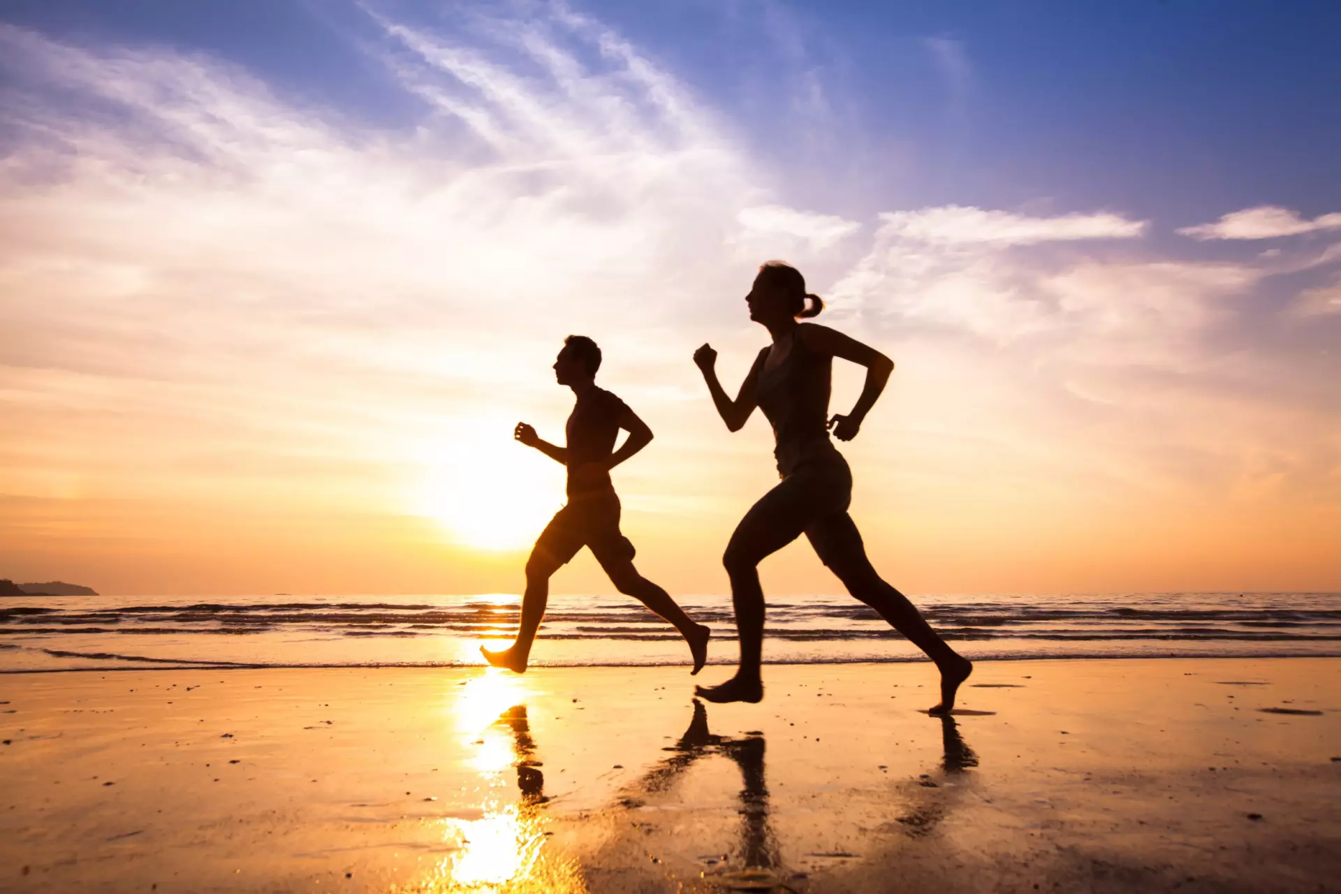 Two people having a healthy lifestyle by running on a beach at sunrise.