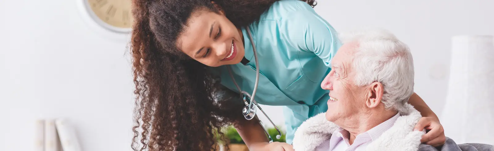 Panorama of a happy nurse with a stethoscope covering an elderly man with a blanket in a nursing home Cost-Effective Surgeons