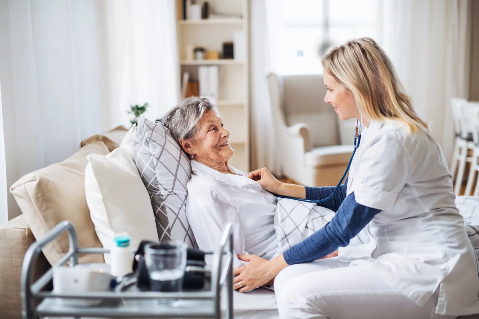 A health visitor examining a sick senior woman lying in bed at home with stethoscope. Outpatient Surgery Centers